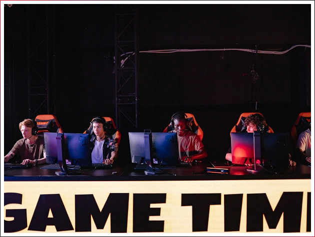 Řada hráčů v sluchátkách sedí u počítačů na pozadí nápisu „GAME TIME“.